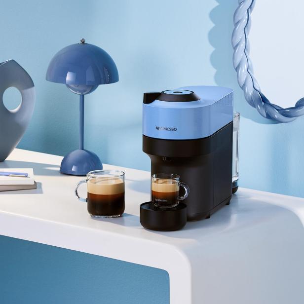 Eine blaue Nespresso-Maschine steht mit zwei Tassen Kaffee auf einem weißen Tisch.