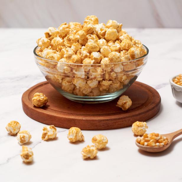 Eine Schüssel mit Karamell-Popcorn steht auf einem Holzteller.