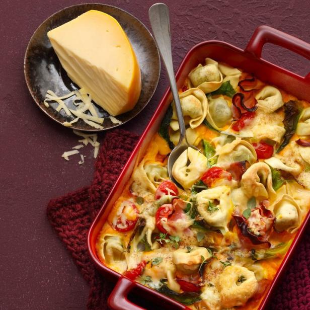 Ein Auflauf mit Tortellini, Tomaten, Spinat und Käse in einer roten Auflaufform.