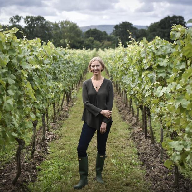 Eine Frau steht in Gummistiefeln in einem Weinberg.