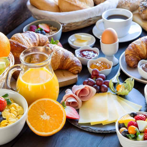 Ein reichhaltiges Frühstück mit Croissants, Obst, Müsli, Wurst, Käse und Kaffee auf einem Tisch.
