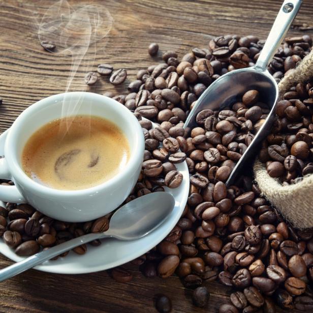 Eine Tasse Kaffee mit Kaffeebohnen und einem Löffel auf einem Holztisch.