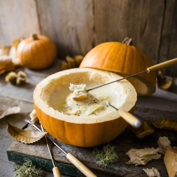 Käsefondue in einem ausgehöhlten Kürbis mit Brotstücken und Fonduegabeln.