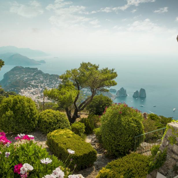 Blick von einem Garten auf Capri mit der Küstenlinie und einer Statue im Vordergrund.