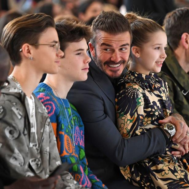 David Beckham umarmt seine Tochter Harper bei einer Modenschau, während seine Söhne neben ihnen sitzen.