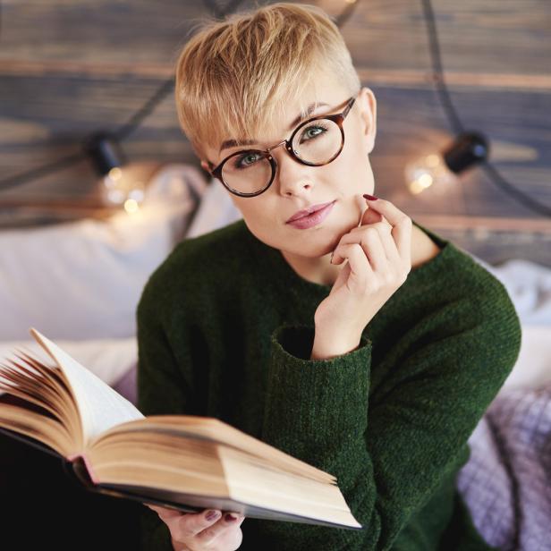 Eine Frau mit Brille liest ein Buch im Bett.