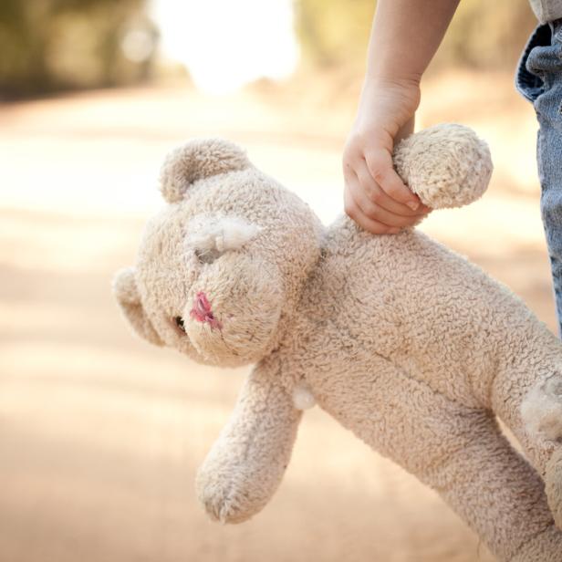 Ein Kind hält einen abgenutzten Teddybären im Arm.