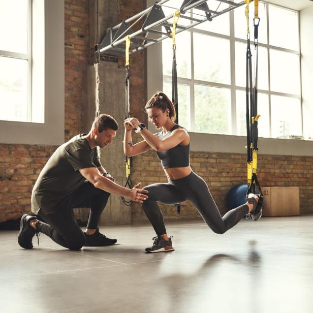Eine junge Frau trainiert mit einem Trainer und TRX-Bändern in einem Fitnessstudio.