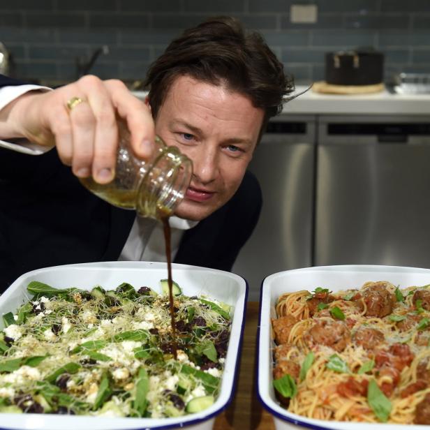 Jamie Oliver beträufelt einen Salat mit Dressing, daneben steht Spaghetti mit Fleischbällchen.