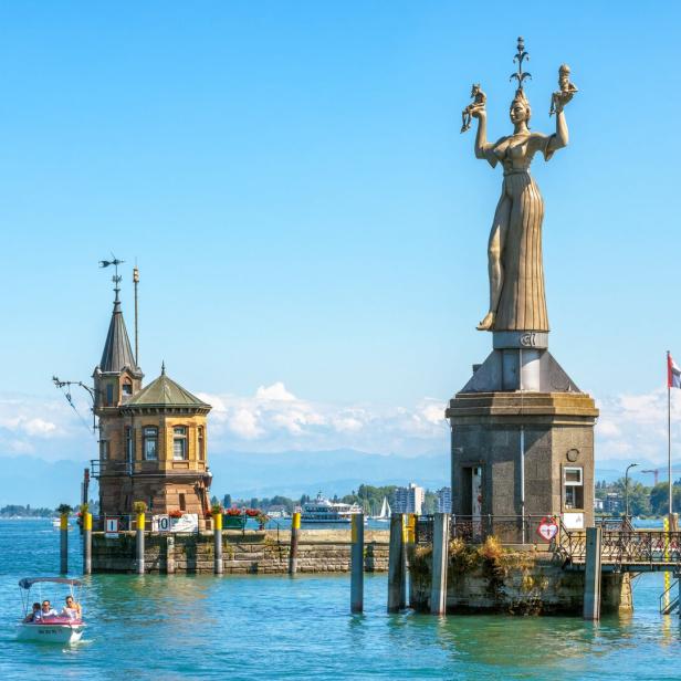 Die Imperia-Statue am Hafen von Konstanz mit dem See und den Alpen im Hintergrund.