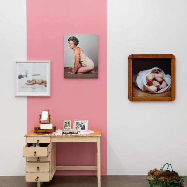 Eine Kunstinstallation mit Fotografien, einem Schminktisch und einem Korb mit Haarteilen.