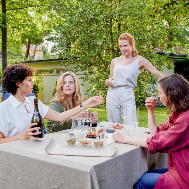 Vier Frauen sitzen im Garten an einem Tisch mit Getränken und Snacks.