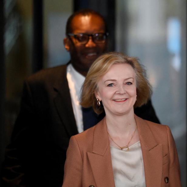 Liz Truss lächelt, während Kwasi Kwarteng im Hintergrund steht.