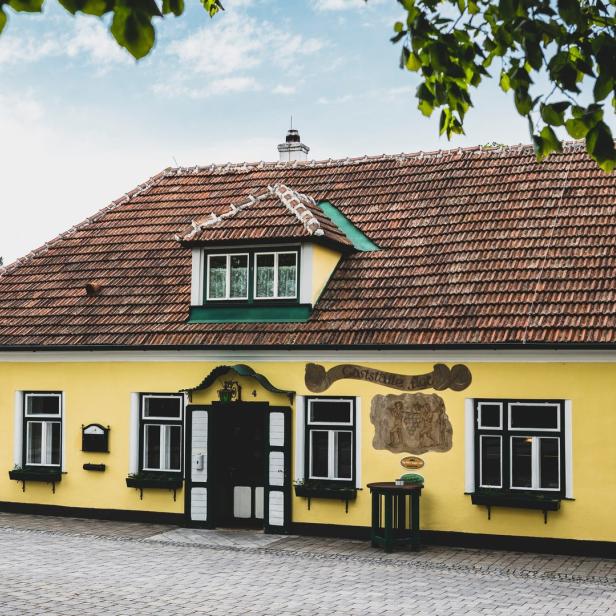 Ein gelbes Haus mit einem roten Ziegeldach und grünen Akzenten.