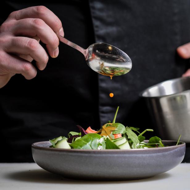 Ein Koch beträufelt einen Salat mit Dressing.