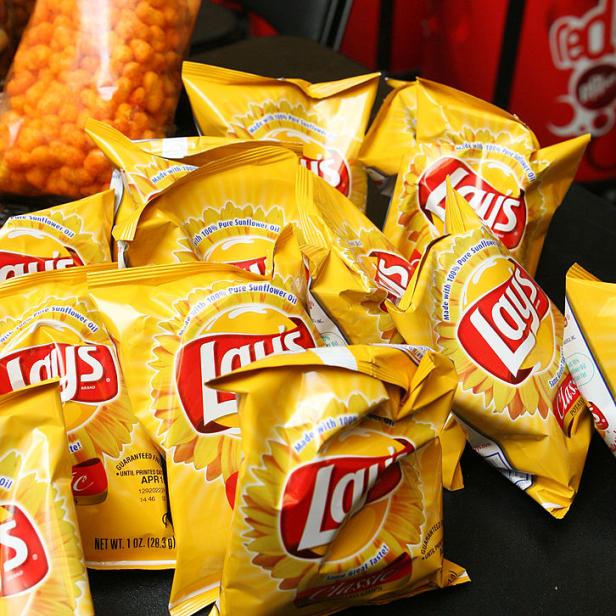 Viele gelbe Tüten Lay's Classic Kartoffelchips liegen auf einem Tisch.