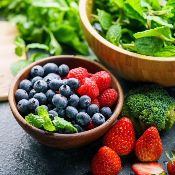 Eine Schüssel mit Blaubeeren und Himbeeren neben anderem Gemüse und Kräutern.