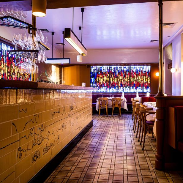Innenansicht eines eleganten Restaurants mit Buntglasfenstern und gedeckten Tischen.