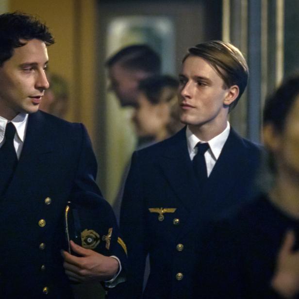 Zwei junge Männer in Marineuniformen stehen in einem Raum.