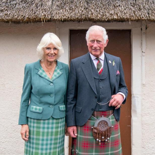 König Charles und Königin Camilla in traditioneller schottischer Kleidung vor einem Gebäude.