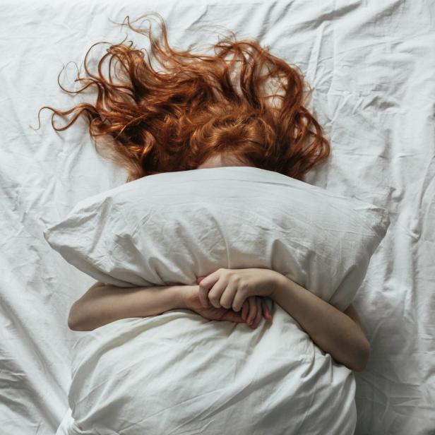 Eine Frau mit roten Haaren liegt mit dem Gesicht auf einem Kissen im Bett.