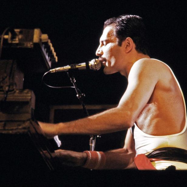 Freddie Mercury von Queen spielt Klavier und singt in ein Mikrofon.