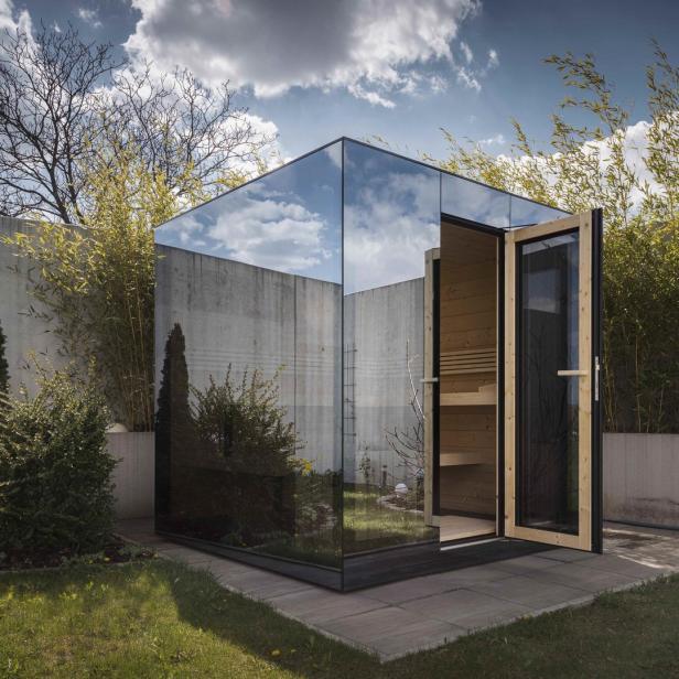 Eine moderne Sauna mit Glaswänden steht in einem Garten.