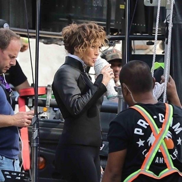 Jennifer Lopez trinkt von einem glitzernden Becher am Set.