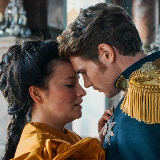 Ein Paar in historischer Kleidung steht eng umschlungen in einem Schloss.