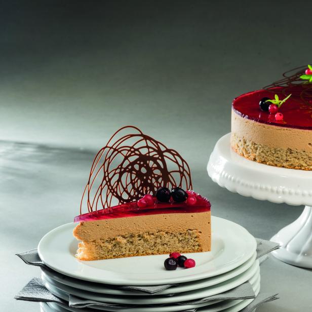 Ein ganzer Kuchen und ein Stück Kuchen sind mit roten Johannisbeeren und Schokoladendekor verziert.