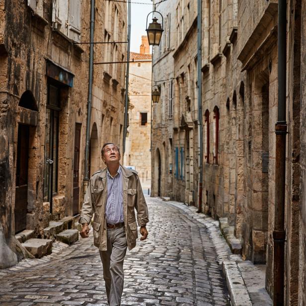 Ein Mann geht eine enge Gasse mit alten Steinhäusern entlang und schaut nach oben.