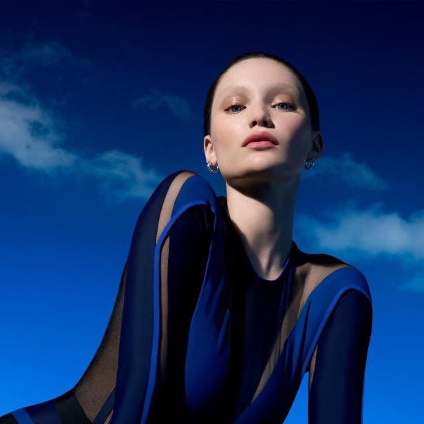 Eine Frau mit blauem Kleid posiert vor einem blauen Himmel.