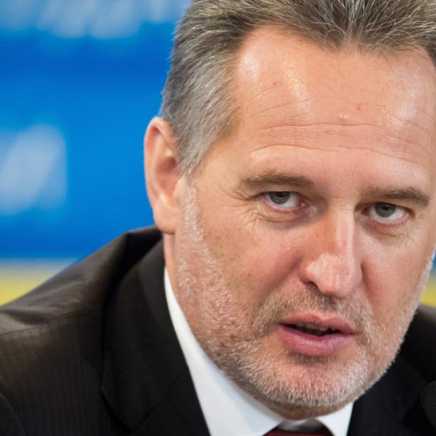 Ein Mann mit grauem Haar und Bart spricht vor einem blau-gelben Hintergrund.