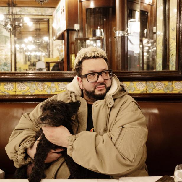 Ein Mann mit Brille hält einen kleinen schwarzen Hund in einem Restaurant.