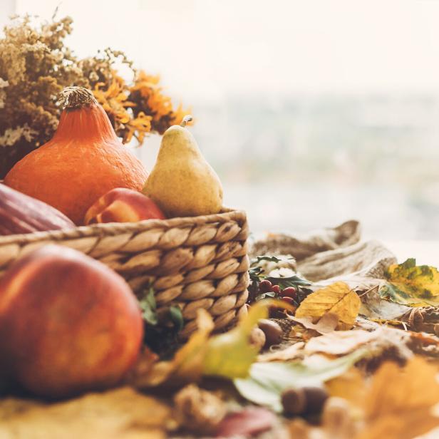 Ein Korb mit Herbstfrüchten und Gemüse, umgeben von bunten Blättern.