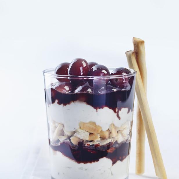 Ein Dessert mit Joghurt, Keksen, Trauben und dunkler Soße in einem Glas.