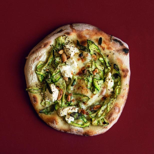 Eine Pizza mit Zucchini, Käse und Mandeln auf einem roten Hintergrund.