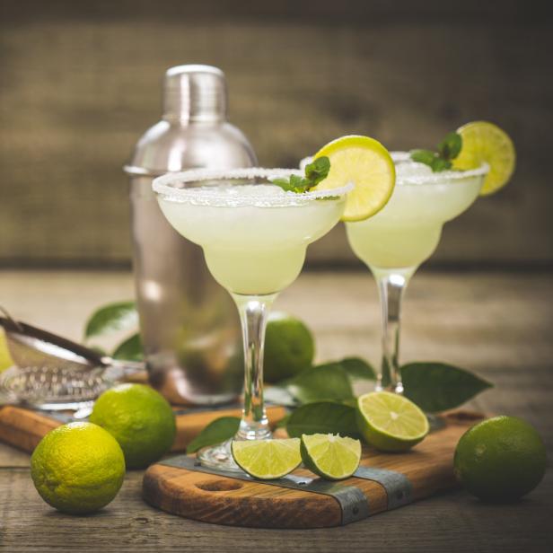 Zwei Margaritas mit Limetten und Minze auf einem Holztisch.