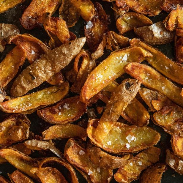 Nahaufnahme von goldbraunen, gebackenen Kartoffelspalten mit grobem Salz bestreut.
