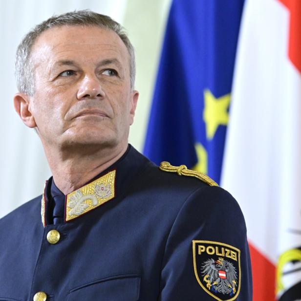 Ein älterer Mann in österreichischer Polizeiuniform steht vor EU- und österreichischer Flagge und blickt ernst zur Seite.