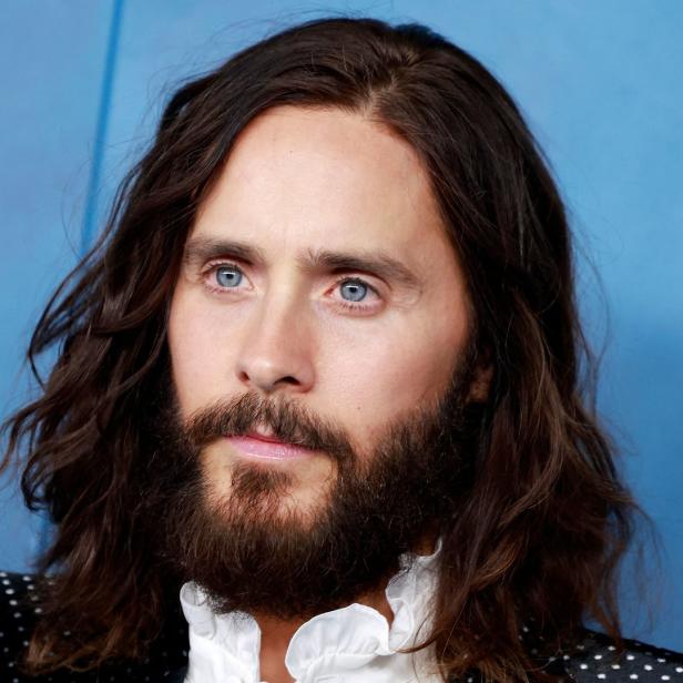 Porträt von Jared Leto mit Bart und langen Haaren vor blauem Hintergrund.