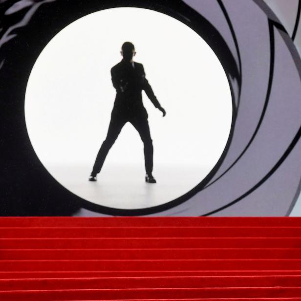 Daniel Craig auf einem roten Teppich vor einer stiliserten Irisblende.