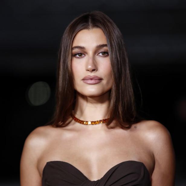 Hailey Bieber trägt ein trägerloses, braunes Kleid und eine bernsteinfarbene Halskette.