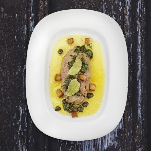 Ein Teller mit Fleisch, Kapern, Croutons und Limettenscheiben in einer hellen Sauce.