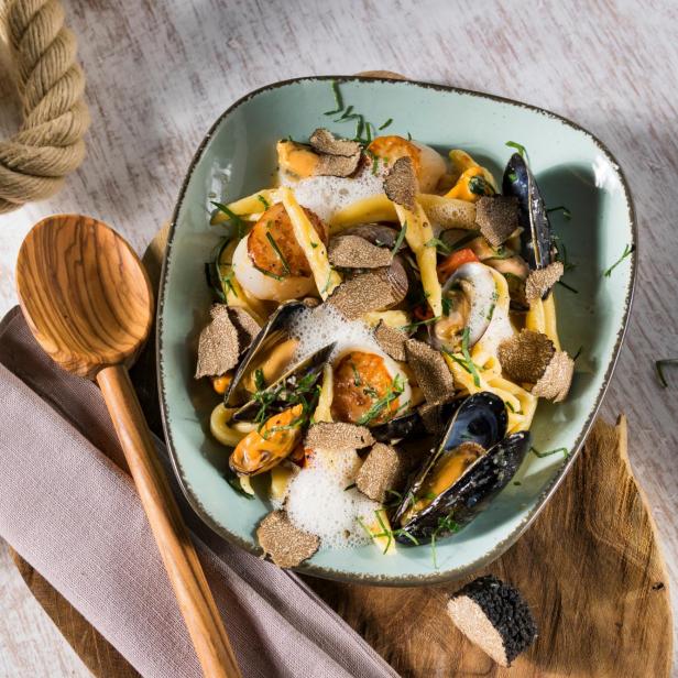 Ein Teller Pasta mit Meeresfrüchten und Trüffeln auf einem Holztisch.