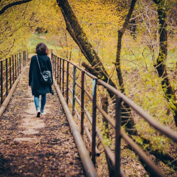 Eine Frau geht auf einer Brücke durch eine herbstliche Landschaft.