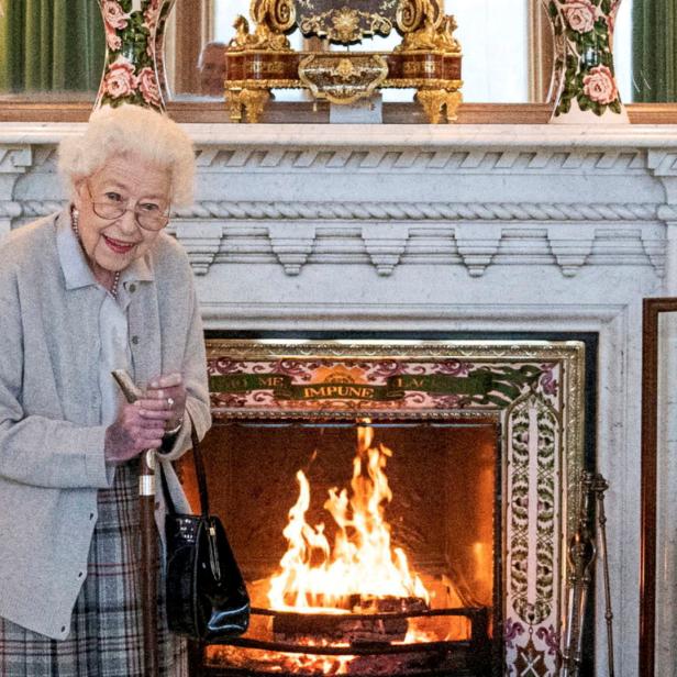 Königin Elisabeth II. steht mit einem Gehstock vor einem Kamin.