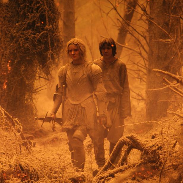 Galadriel und ein junger Mann stehen in einer zerstörten Waldlandschaft.