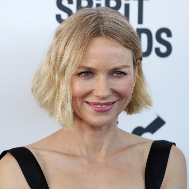 Naomi Watts lächelt in einem schwarzen Kleid.