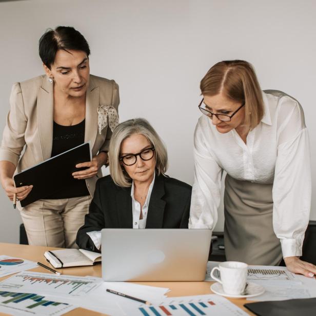 Drei Geschäftsfrauen arbeiten gemeinsam an einem Tisch mit Diagrammen und einem Laptop.